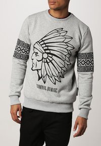 Grey sweatshirt made of soft fabric featuring a black graphic of a Native American chief's head and patterned accents on the sleeves.