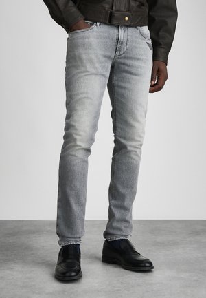 Lysegrå denimjeans med slim fit, der har slidte områder og klassisk femlomme-design. Båret med sorte lædersko.