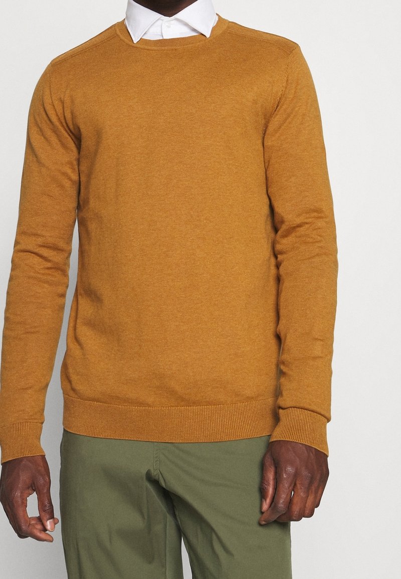 Maglione giallo senape realizzato in morbido materiale a maglia. Presenta una scollatura a girocollo e polsini a coste. Abbinato a pantaloni verdi.