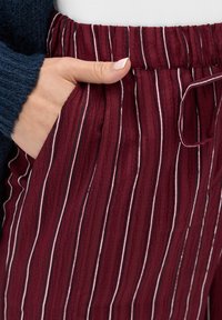 Spodnie w burgundowym kolorze w paski, wykonane z fakturowanej tkaniny, z elastycznym pasem i bocznymi kieszeniami, zdobione cienkimi białymi i czarnymi liniami.