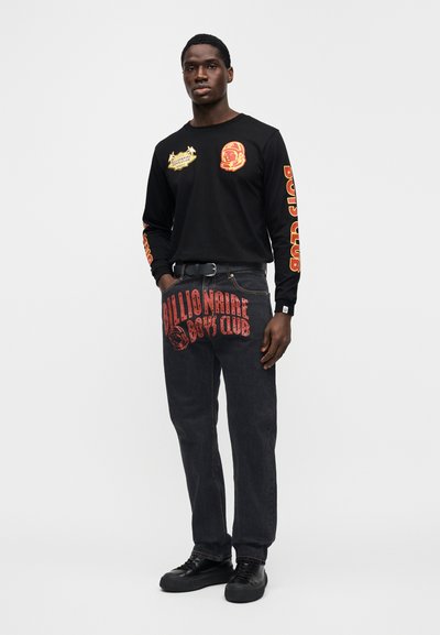 Μακρυμάνικο μαύρο πουκάμισο με κίτρινα και κόκκινα γραφικά στα μανίκια, συνδυασμένο με σκούρο τζιν με το κείμενο και το γραφικό "Billionaire Boys Club".