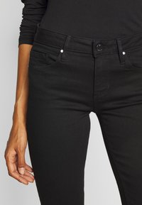 Černé džíny z denimu s klasickým pětipocketovým designem, slim fit a kovovými detaily včetně knoflíku a nýtků. Hladká textura.