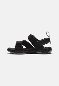 Sandal preto com tiras ajustáveis, sola almofadada e palmilha texturizada. Forma arredondada com uma alça na parte de trás para facilitar o calçar.
