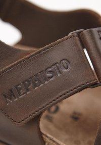 Brązowe skórzane sandały z regulowanym paskiem, z wytłoczonym logo "Mephisto" i teksturowaną powierzchnią, otwarty design zapewniający wentylację.