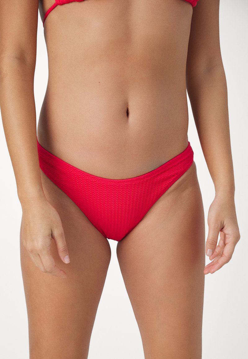Costum de baie de jos roșu cu un model texturat, design cu talie joasă și material neted. Prezentă o tăietură moderată fără elemente metalice suplimentare.