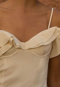 Beige šaty se strukturovaným výstřihem ve tvaru srdce, s volánkovým překrytím a tenkými ramínky, vyrobené z hladkého materiálu.