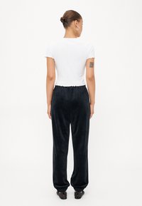 Hvit ribbet crop-top med korte ermer, sammen med løstsittende svarte fløyels joggebukser med elastisk liv og mansjetter.