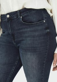 Dark blue denim jeans with a straight cut, featuring front pockets, slight fading on the thighs, and silver button hardware.