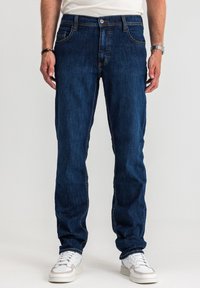 Ciemnoniebieskie dżinsy z denimu o prostym kroju, z delikatnymi detalami przeszyć, pięcioma kieszeniami oraz zapięciem na guziki. W połączeniu z białymi trampkami.