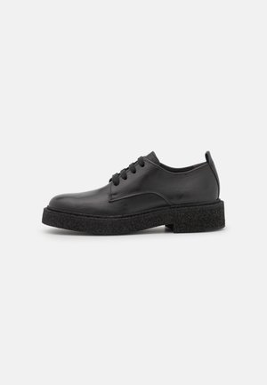 Chaussure en cuir noir à lacets avec semelle épaisse et texturée et petit talon, vue de profil sur un fond clair uni.
