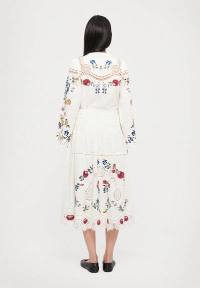 Weißes Kleid mit aufwendiger floraler Stickerei in Rot, Blau und Gelb. Hat lange Ärmel, Spitzenakzente und eine geraffte Taille.