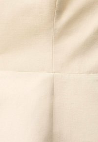 Beige tyg med en subtil textur, som har stygn som skapar geometriska former. Slät yta med en ljus, neutral nyans.