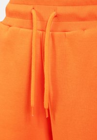Helle orange Sweatpants mit einem gerippten Bund und einem Kordelzug, der eine geflochtene Textur aufweist. Das Material wirkt weich und glatt.