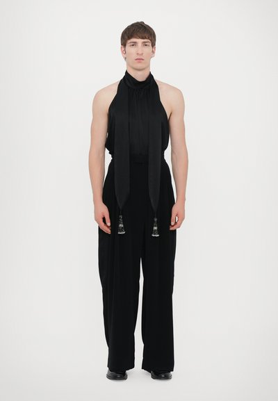 Sort outfit bestående af en ærmeløs halterneck-top med draperet hals og lang tørklæde, parret med vide benbukser og udsmykkede frynser.