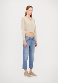 Maglione beige cropped con scollo a V, orlo a coste, abbinato a jeans baggy azzurri e sneakers beige con una finitura testurizzata.
