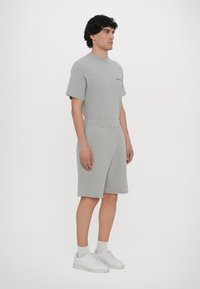 Gray cotton short-sleeve jumpsuit with a crew neck and a relaxed fit, featuring a waistband and hemmed shorts, layered over white sneakers.