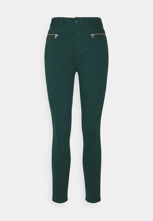 Dunkelgrüne Skinny-Jeans aus elastischem Stoff, ausgestattet mit zwei Reißverschlusstaschen vorne und einem Knopfverschluss an der Taille.