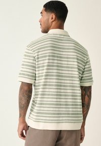Camisa polo a rayas en verde claro y crema, con mangas cortas, cuello acanalado y una textura sutil en la tela.