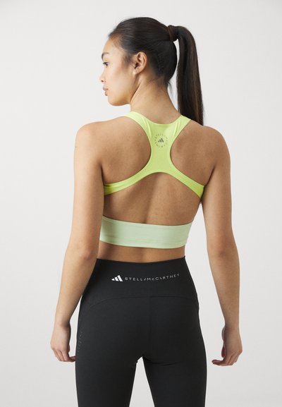 Sportski crop top u svijetlozelenoj boji s racerback dizajnom i izrezima, u kombinaciji s crnim tajicama visokog struka s logotipom.