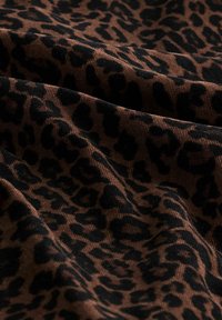 Hnedá tkanina s leopardím vzorom v čiernej farbe, s textúrovaným povrchom a mäkkými, plynulými záhybmi.
