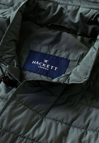 Gepolsterte Jacke in Dunkelgrün mit gesteppter Textur. Innenetikett mit der Aufschrift "HACKETT LONDON" auf dunkelblauem Hintergrund.