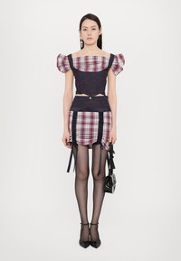 Plaid crop top with puff sleeves, dark blue fabric accents, and a matching plaid skirt; features lace-up details and black high heels.