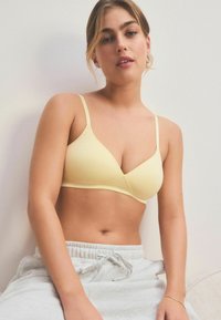 Sutien wireless de un galben deschis, cu o textură netedă și o formă triangulară. Bretele subțiri, ajustabile, cusături minime și un design fără cusături.