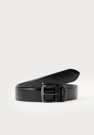 Ceinture en cuir noir roulée avec une boucle à ardillon métallique noire, sur un fond clair uni.