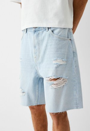 Shorts en denim bleu clair avec une coupe décontractée, présentant plusieurs zones déchirées et des ourlets effilochés. Design classique à 5 poches.