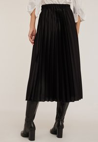 Gonna midi plissettata nera con vita elastica, realizzata in un tessuto lucido, caratterizzata da pieghe verticali e una texture liscia.