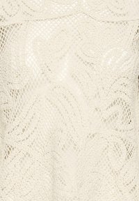 Tissu en dentelle couleur crème avec des motifs floraux et feuillus complexes tissés dans un fond en maille fine.