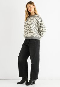 Gray and cream striped sweater with a loose fit, paired with black wide-leg jeans and black heeled ankle boots.