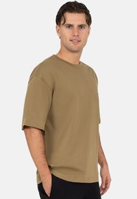 Olijfgroene korte mouw t-shirt gemaakt van zachte stof; heeft een ronde hals en een ontspannen pasvorm met zichtbare stiksel-details.