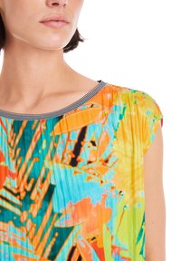 Bunte Bluse mit einem abstrakten Blumenmuster in Orange, Türkis und Grün. Faltentextur mit einem schwarz-weißen gestreiften Ausschnitt.