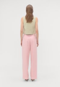 Kort olivgrønn tanktop kombinert med høytlivede pastellrosa vide bukser. Glatt stoff, minimalistisk design og subtile detaljer.