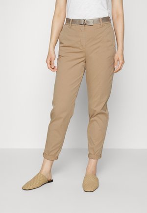 Pantaloni in cotone beige con una vestibilità rilassata, con risvolti e una cintura coordinata. Indossati con scarpe slip-on intrecciate color nocciola.