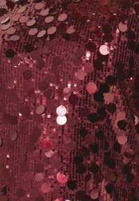 Röd paljett på tyg med cirkulära paljetter som reflekterar ljus, vilket skapar en texturerad, glittrande yta. Övergripande slät och glänsande utseende.