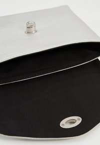 Pochette in argento con texture, dotata di chiusura a scatto metallica. L'interno presenta una fodera in tessuto nero e un dettaglio ovale in metallo alla base.