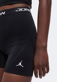 Gros plan d’une personne portant un short de sport Jordan noir avec le logo Jumpman et une ceinture avec la marque Jordan.