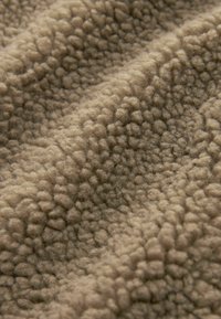 Tan fleece stof met een textuur, kenmerkend door kleine, verhoogde vezels die een zachte, gezellige uitstraling creëren.