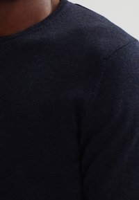 Mörkblå stickad tröja med rund halsringning, tillverkad av mjukt material, med sömlösa sömmar och en slät yta.