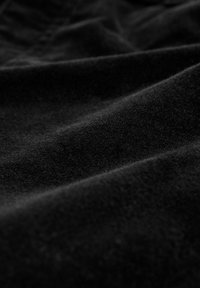 Černá tkanina s jemným, texturovaným povrchem, vykazující mírné záhyby a křivky, které zdůrazňují její hladký, matný vzhled.