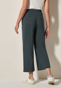 Pantalons larges vert foncé avec une taille élastique et deux poches arrière. Associés à des baskets blanches avec des accents verts.