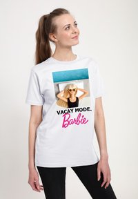 Bílé tričko s barevným potiskem panenky Barbie v brýlích. Text zní "REŽIM DOVOLENÉ. Barbie" v černých a růžových písmenech.