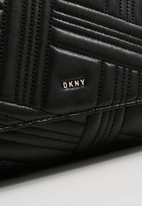 Surface en cuir matelassé noir avec des surpiqûres verticales et horizontales et un petit détail du logo DKNY en métal doré.