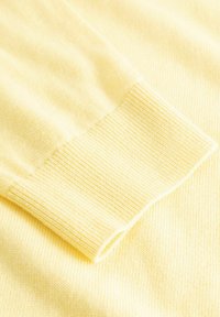 Détail d'un pull jaune montrant un poignet côtelé et une texture lisse, avec un gros plan sur le tissu tricoté doux.