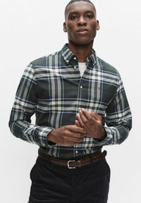 Zielono-granatowa koszula w kratę na guziki z białymi, szarymi i czerwonymi akcentami, z kołnierzykiem i haftowanym logo na piersi. Brązowy pleciony pasek.