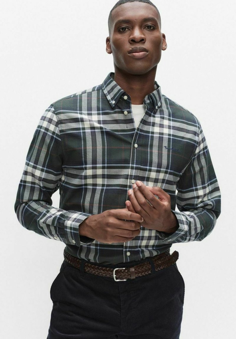 Zielono-granatowa koszula w kratę na guziki z białymi, szarymi i czerwonymi akcentami, z kołnierzykiem i haftowanym logo na piersi. Brązowy pleciony pasek.