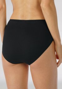 Vysoko seříznuté černé bikinové kalhotky vyrobené z hladkého materiálu, s bezešvým designem a zakřivenými otvory na nohy pro bezpečné nošení.