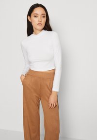 Top blanc à manches longues cropped avec un col montant, associé à un pantalon large à rayures verticales marron, avec poches latérales et une coupe décontractée.